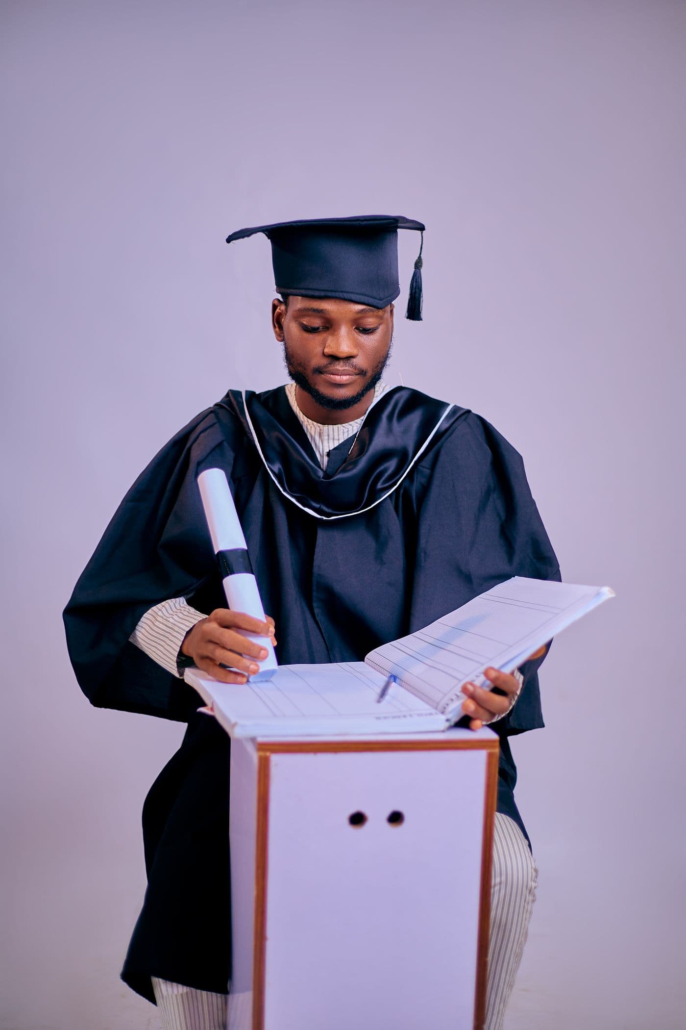 A young graduate in a cap and gown holds a diploma.