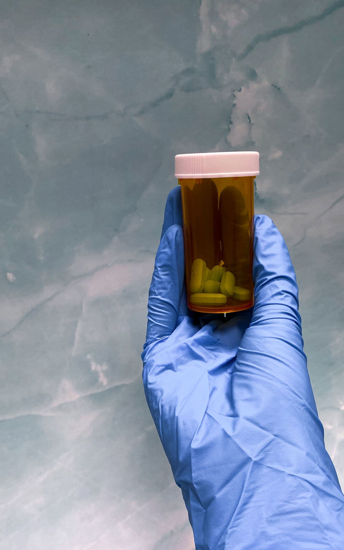 A gloved hand holds up an amber prescription bottle.
