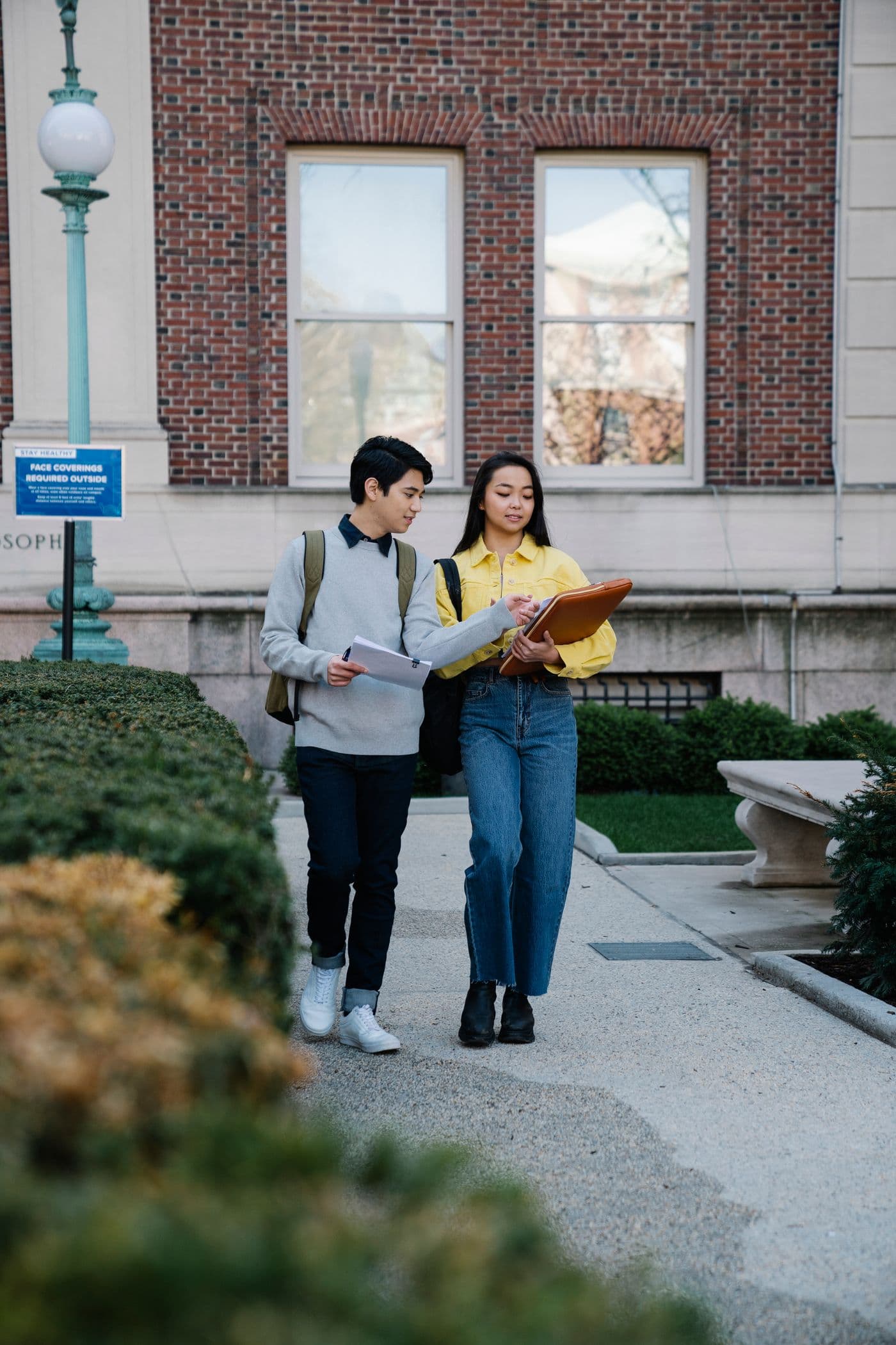 Two students carrying folders walk along a campus path.