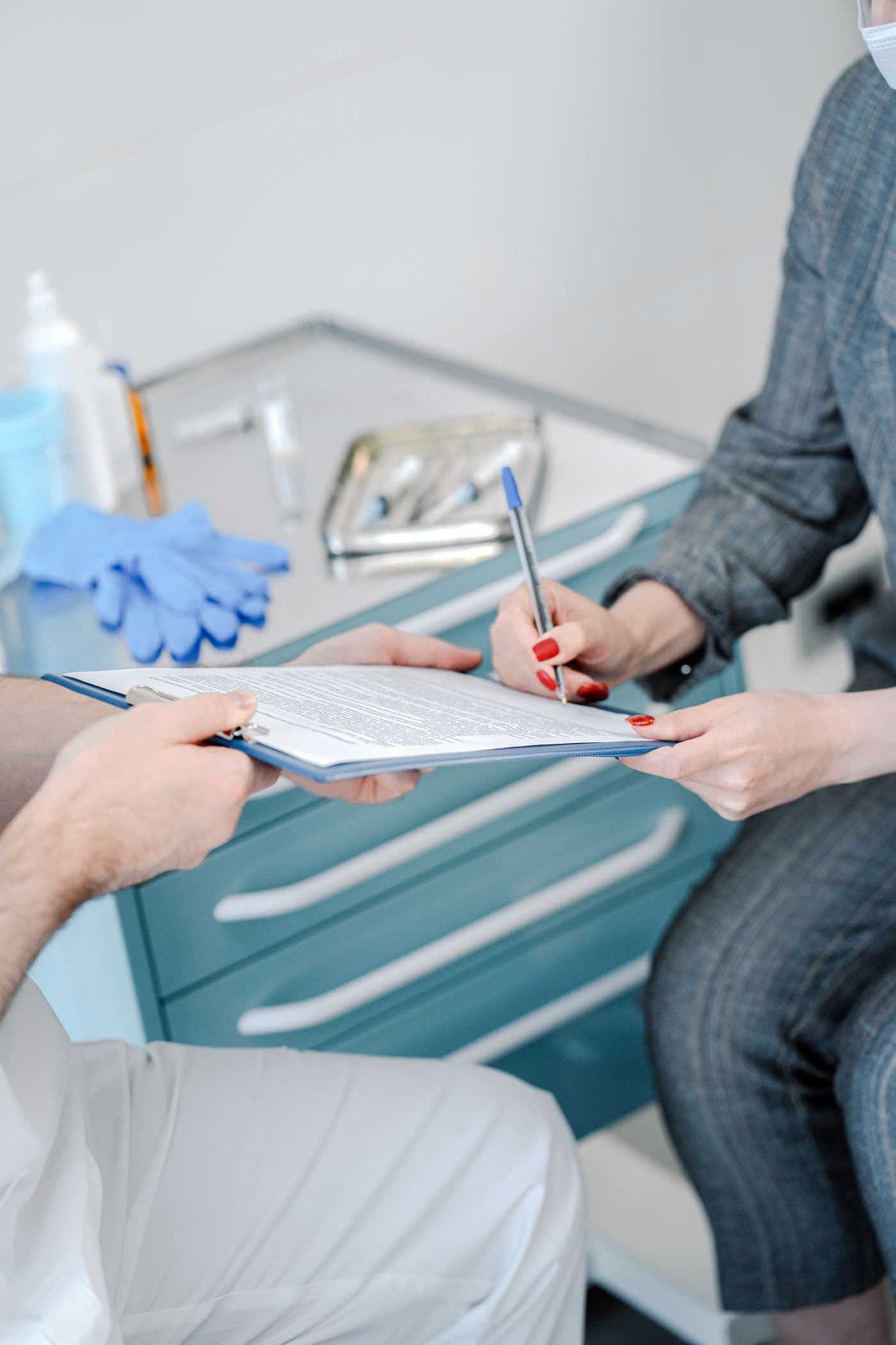 A clinician holds a clipboard while a patient signs a form.
