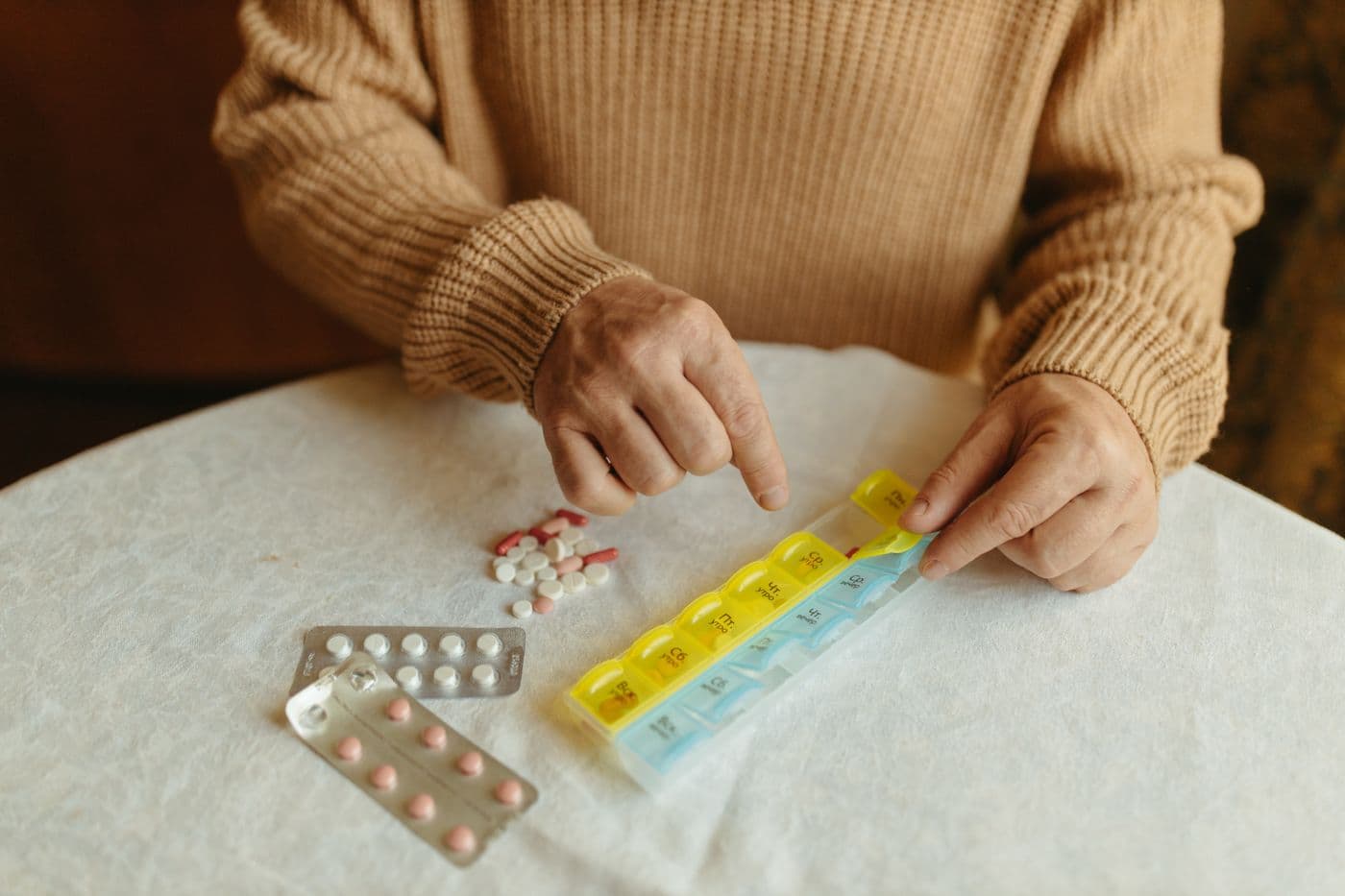 An older person sorts tablets into a weekly pill organizer.