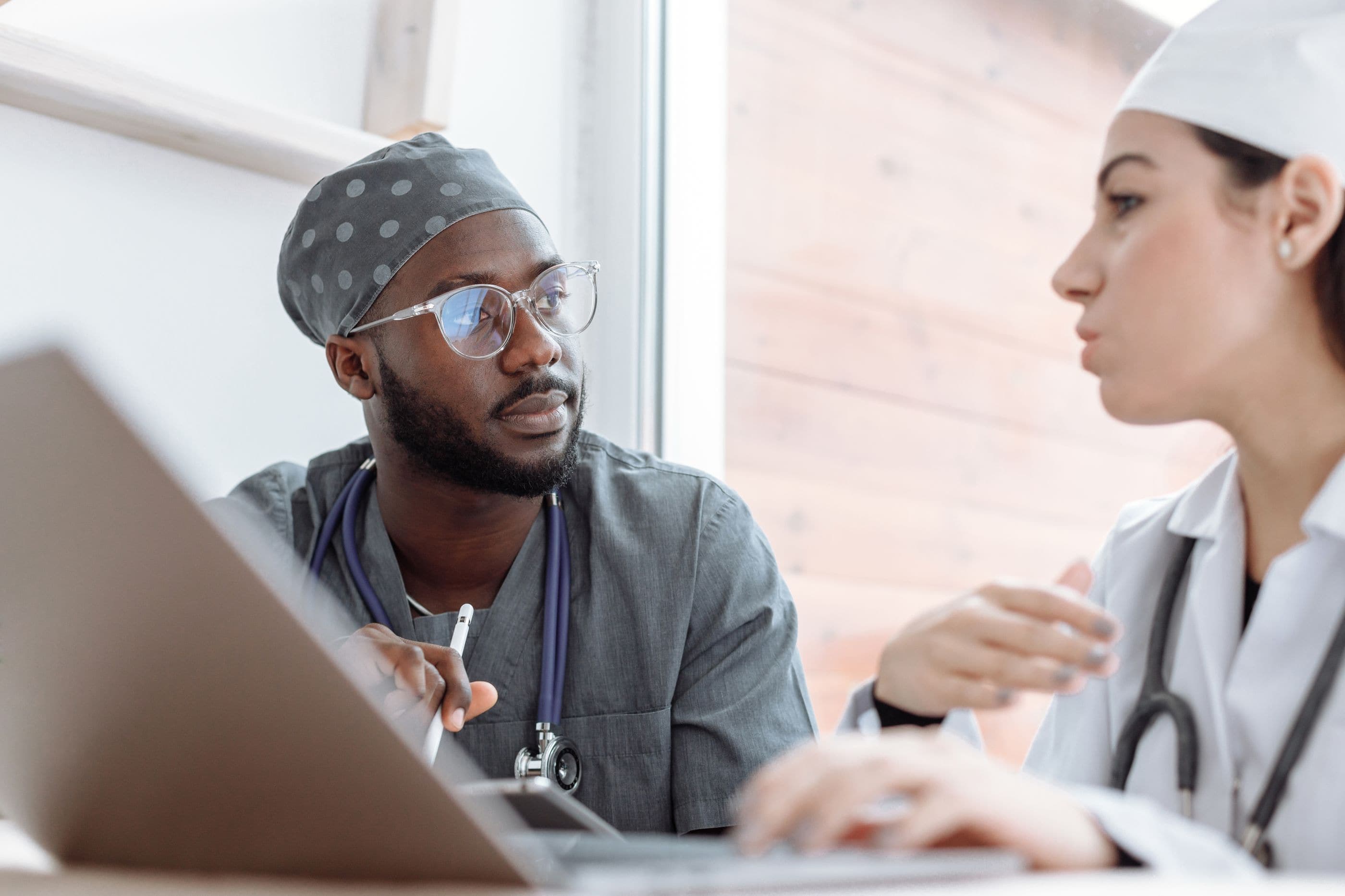 Two clinicians talk across a laptop at a desk.