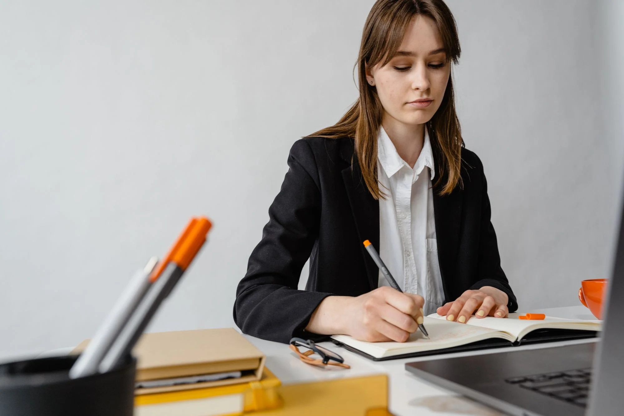 A professional writes in a notebook beside her laptop.