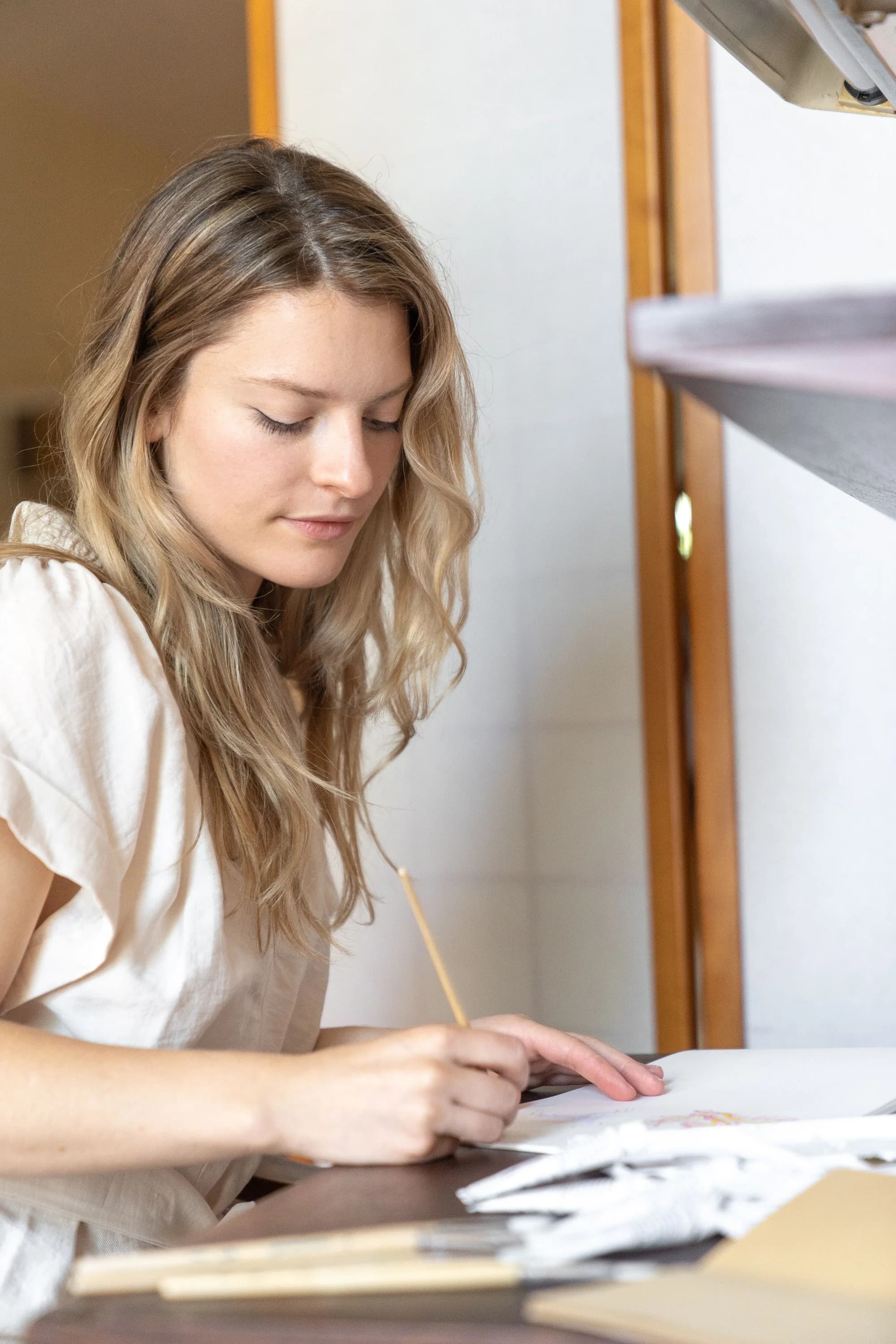 A woman writes in a notebook at a bright desk.