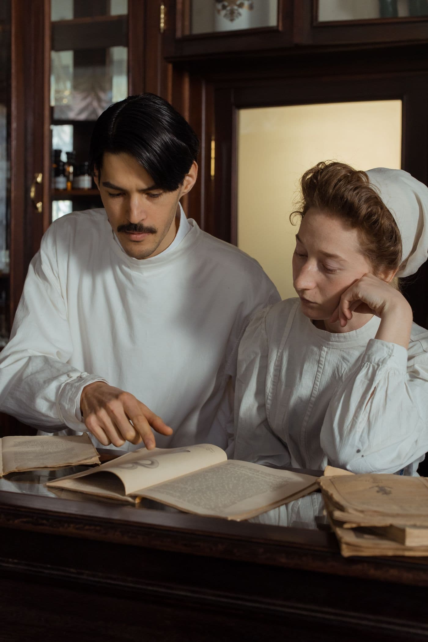 Two pharmacists read a reference book together at a counter.